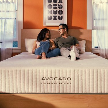 Avocado Eco Organic Mattress in a bedroom with orange walls with a man and a woman sitting on it