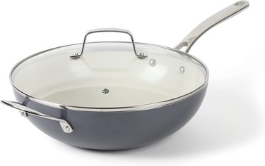 A gray 12 inch pan, with a white bottom and a clear lid with a silver handle rests in front of a white background.