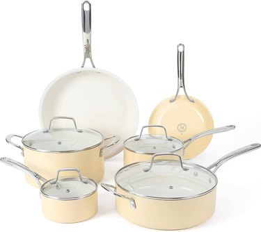 An eight and ten inch frying pan, a 1 quart covered sauce pan, a 2.5 quart covered sauce pan, a 4.6 quart covered sauce pan and a 5.5 quart covered dutch oven, all in the color butter cream are displayed in front of a white background.