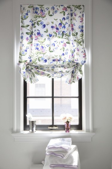 Bathroom window with floral Roman shade and bud vase on the windowsill.