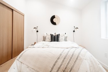 A minimalist bedroom with black and white pillows and a wood bypass closet door
