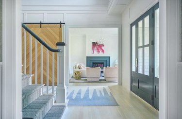Modern traditional entryway with black door, light-wood flooring, blue and white squiggle rug, and hot pink palm frond statement wall art in the background.