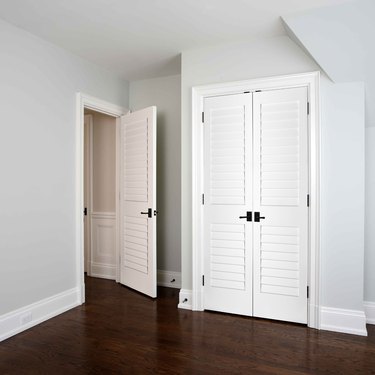 A white louvered bedroom door in a room with wood floors and white louvered closet doors