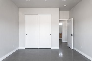 Light gray wall room with white bypass closet doors and dark gray flooring