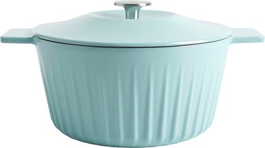 A light blue cast iron dutch oven with ridges is displayed in front of a white background.