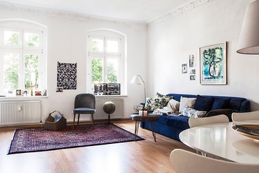 room with white walls, wood floor, blue couch, and purple rug