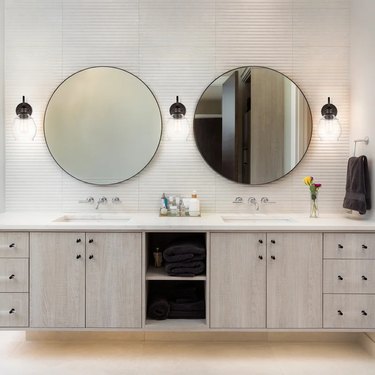 bathroom double vanity with three wall sconces and two round mirrors