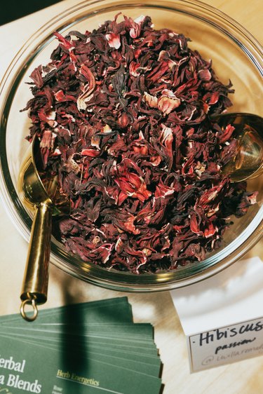 A clear bowl full of hibiscus with a gold spoon.