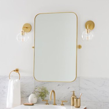 brass-framed pivot mirror over bathroom sink