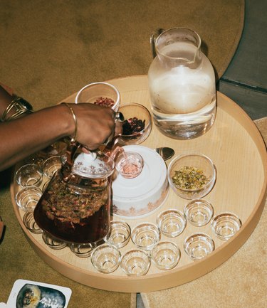 A hand pouring tea into clear glass cups on a tan tray.