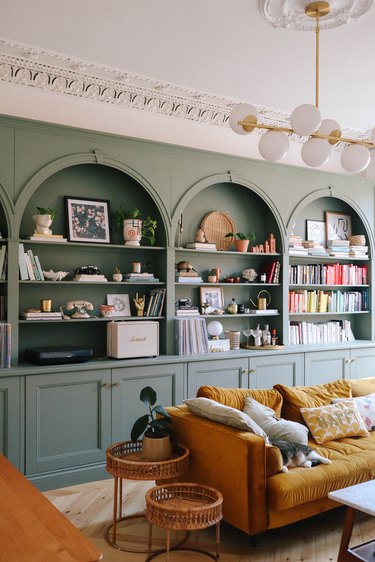 Living room with sage green bookshelves and a yellow couch.