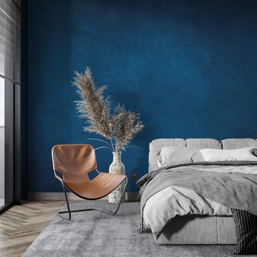Blue accent wall in bedroom with contemporary gray bed and white vase and light brown leather chairecarper with