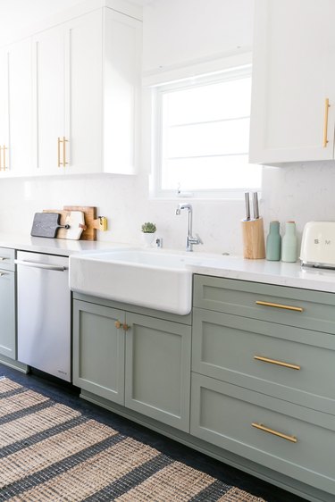 Kitchen with sage green and white cabinets with gold hardware