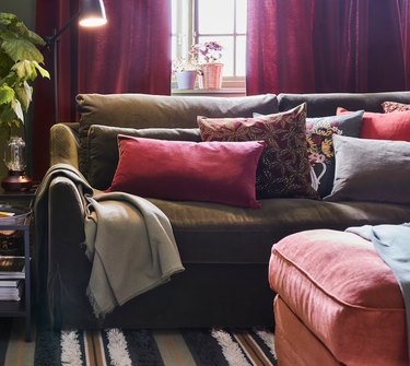 Living room with pink ottoman, pillows, green velvet slipcovered sofa.