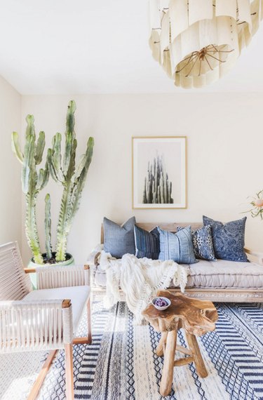 Boho living room with couch, pillows, rug, pendant, chairs, coffee table, large cactus.