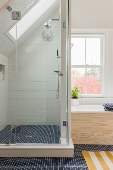 Bathroom with nautical aesthetic, including themed shower light, blue floor tiles, light-wood tub surround, and yellow and white striped floor mat