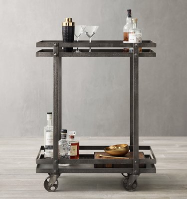 Brushed metal industrial bar cart, glassware, bottles, cocktail shaker.