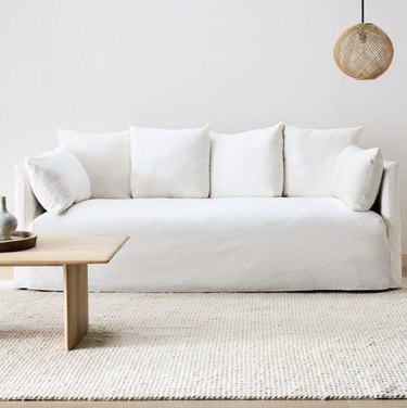 West Elm Shelter Skirted Slipcover Sofa in white in a living room with white walls