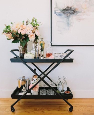 Black metal bar cart with floral arrangement, glassware and bottles.