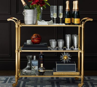 Brass finish bar cart with glassware, bottles.