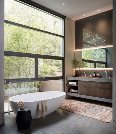 Contemporary bathroom with glass wall, sleek white bathtub, and vanity with cove lighting