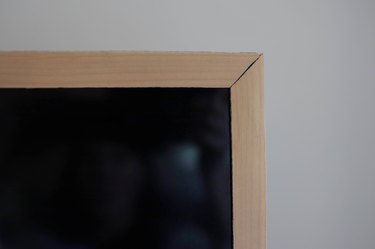 Wood veneer adhered around television trim with mitered corners