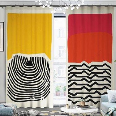 Red, yellow, and black patterned curtains in living room with light blue couch and white table on top of patterned carpet