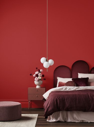 Bedroom with red wall and decorative burgundy headboard and comforter, with mauve side table  floor cushion