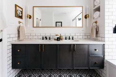 Black and white bathroom with white subway tile, black vanity, mosaic tiled floor, and brass accents
