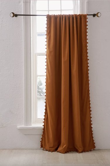 burnt orange curtain with pompoms around the edge