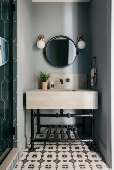 Eclectic bathroom with contemporary cream vanity, brass and white bulb sconces, mosaic tile, and industrial piping vanity base.