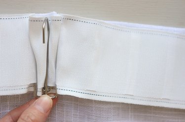 Inserting pleater hook into pleater tape on back of curtain