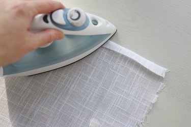 Ironing double hem on white linen fabric