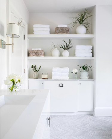 White bathroom with large built-in shelving and cabinet, white sink, and plants