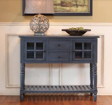 Gray console table with drawers and shelf, art, bowl, lamp.