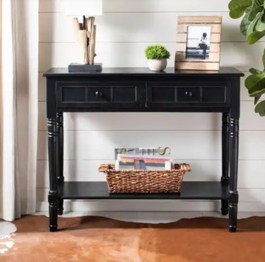 Black console table with drawers, shelf, basket, plant, photo.