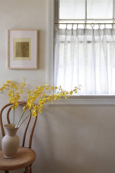 White pinch pleat cafe curtain hanging in window next to picture and yellow flowers