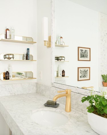 Bathroom sink area with open mirrored shelves, mirror, brass faucet.