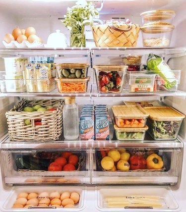 Food and drinks organized in clear bins and baskets inside a refrigerator.