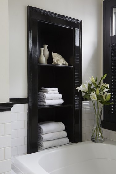 Bathroom shelf painted in high-gloss black paint styled with towels and small vessels in a black and white bathroom