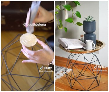On the left is a hand gluing a circular base on a wire geometrical shape. On the left is a geometric side table topped with a book, coffee mug, and a plant.