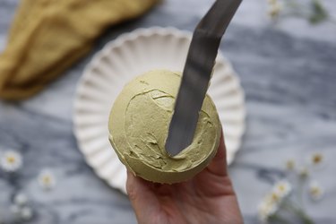 Smoothing sage green frosting onto cupcake with an offset spatula