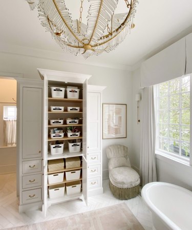 Bathroom with built-in storage cabinets, accent chair, chandelier, tub, rug.