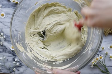 Stirring olive green food coloring into bowl of buttercream frosting