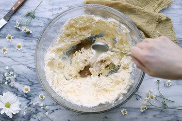 Pouring a tablespoon of milk into bowl of butter and powdered sugar