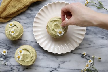 Garnishing sage green frosted cupcakes with chamomile flowers