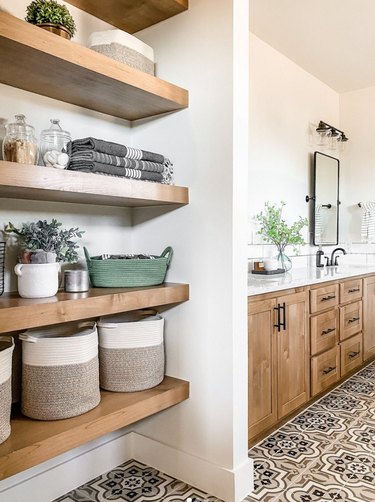 Modern farmhouse bathroom with open shelves, patterned tile floor, wood cabinets.