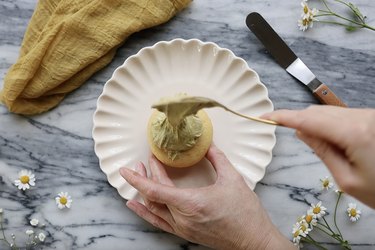 Spooning a dollop of sage green frosting onto center of a cupcake