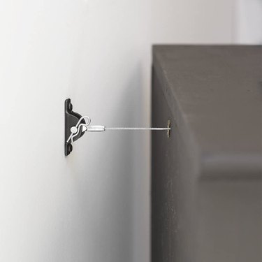 A metal furniture anchor kit attached to a dresser