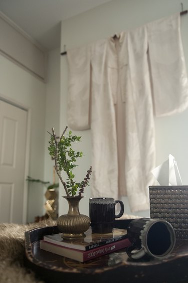 A vintage wedding kimono hanging on the wall near a table with a plant and mug